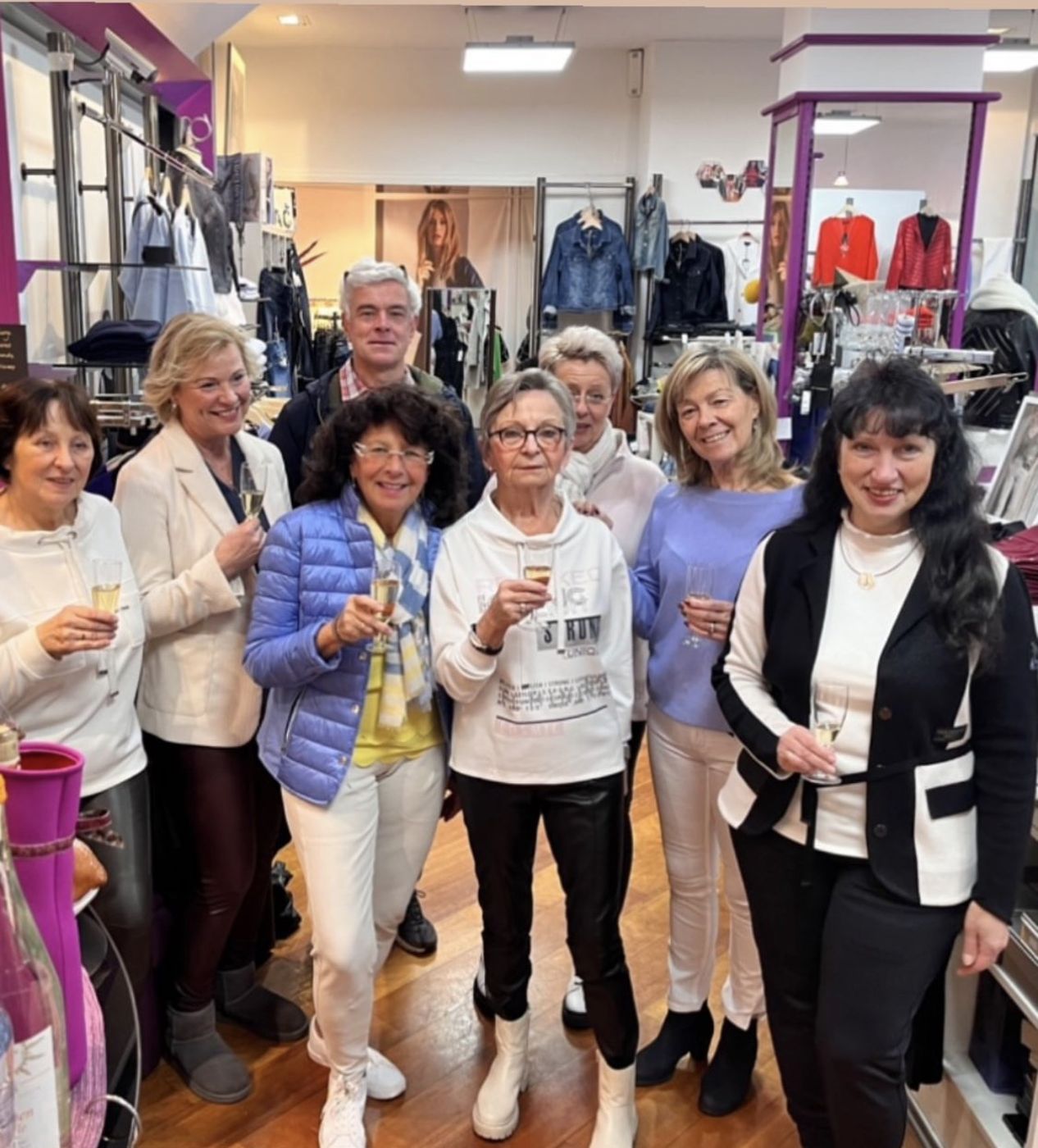 Kundinnen und Team stoßen mit Sekt im Laden an